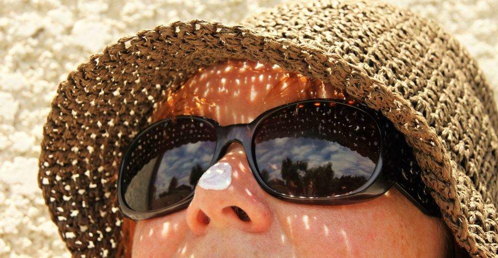 Frau mit Sonnenhut, Sonnenbrille und Sonnencreme, Hautschutz